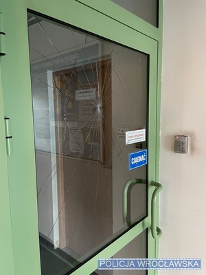 Zdjęcie rozbitej szyby w drzwiach przy wejściu do Komisariatu Policji Wrocław-Osiedle.