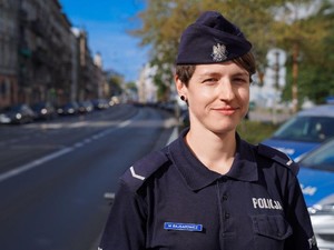 Zdjęcie umundurowanej policjantki stojącej przy jednej z wrocławskich ulic.
