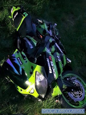 Na zdjęciu przewrócony motocykl marki Kawasaki leżący na trawniku.