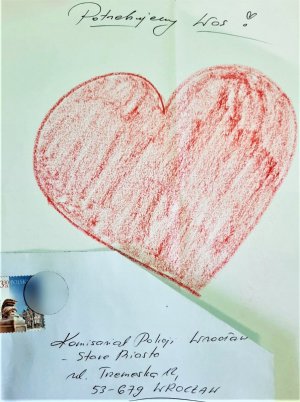 Zdjęcie przedstawia kartkę z rysunkiem przedstawiającym czerwone serce oraz napisem &quot;potrzebujemy was&quot;. Poniżej kartki znajduje się koperta z adresem komisariatu policji Wrocław-Stare Miasto
